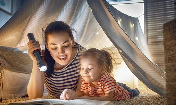 daughter and mother reading a book using a hand lamp perks of work at home jobs