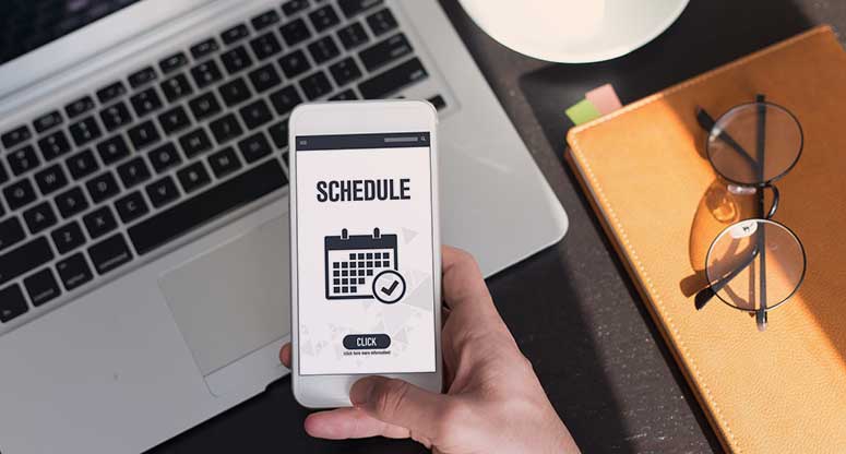 holding a mobile phone with schedule screen on computer background