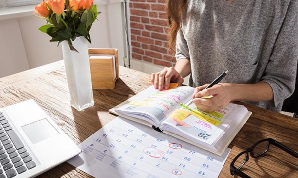 woman working from home writing on agenda and calendar her goals