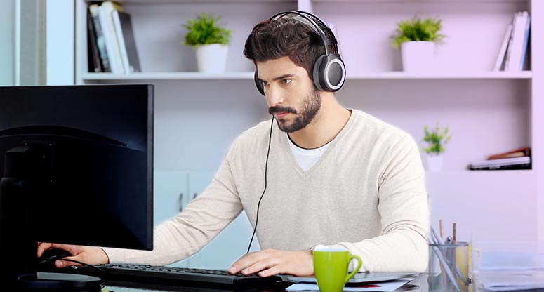 man working from home on desktop and listening to music to keep focused