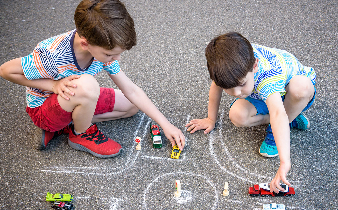 Two little boys playing with toy cars on a chalk-drawn intersection