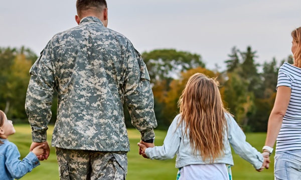 Military family holding hands in a field with their backs turned to the viewer