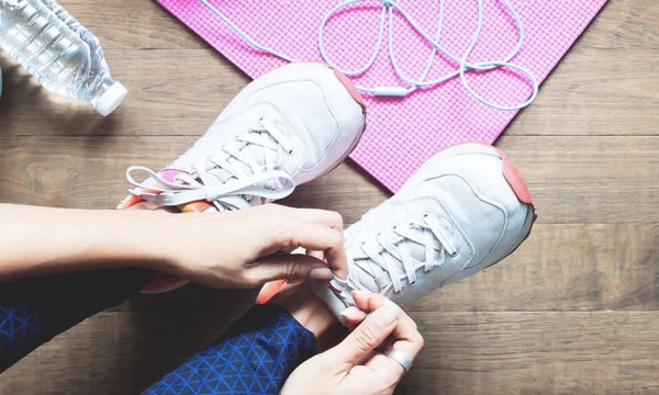 Bird's eye view of a person putting on workout shoes and adorned with headphones, weights, and a yoga mat
