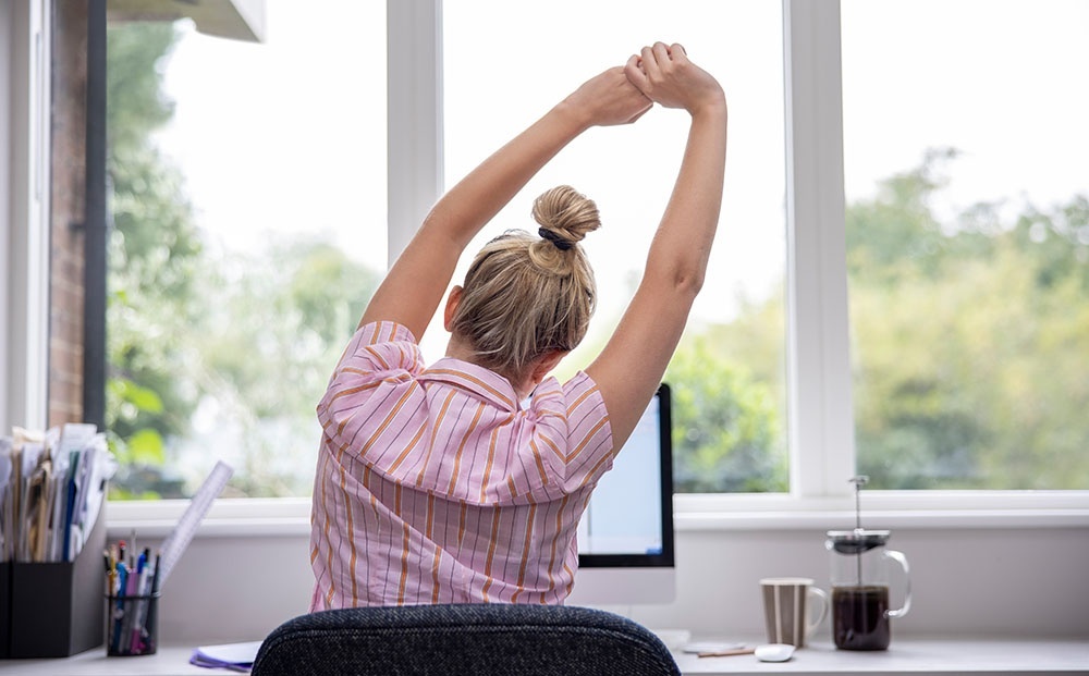 Back shot of a woman stretching her arms at her desk