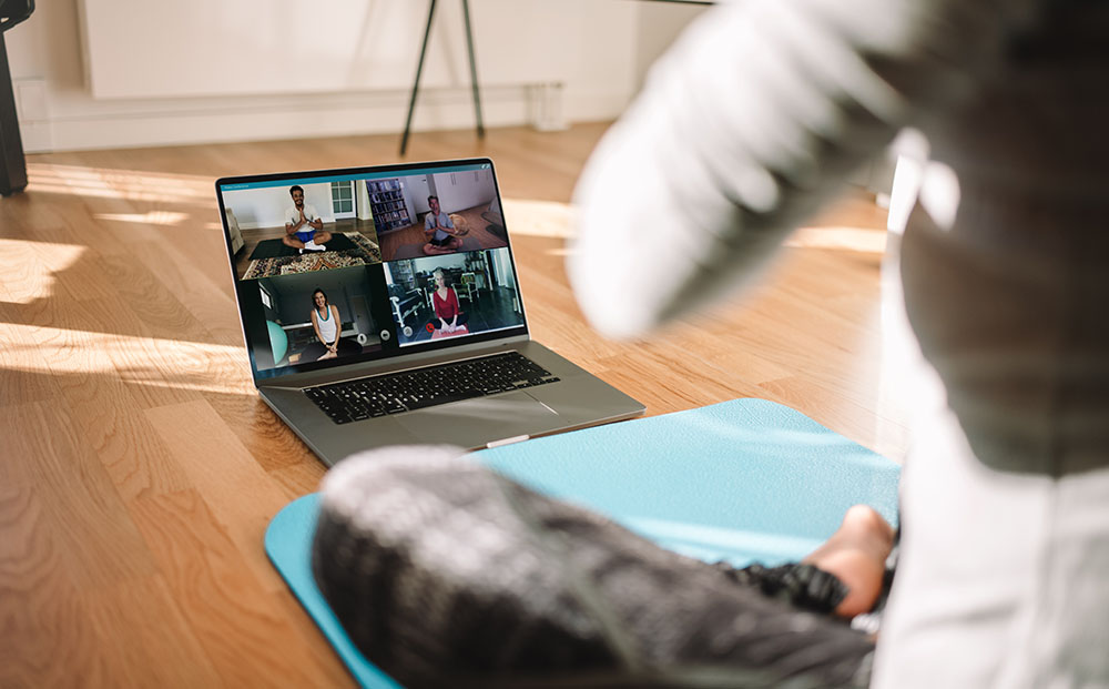 Woman prepares for online yoga class on her mat and a laptop displaying images of other practicers