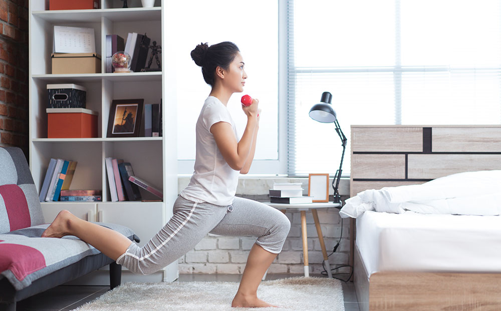 Asian woman exercises in her home using weights and a couch as props