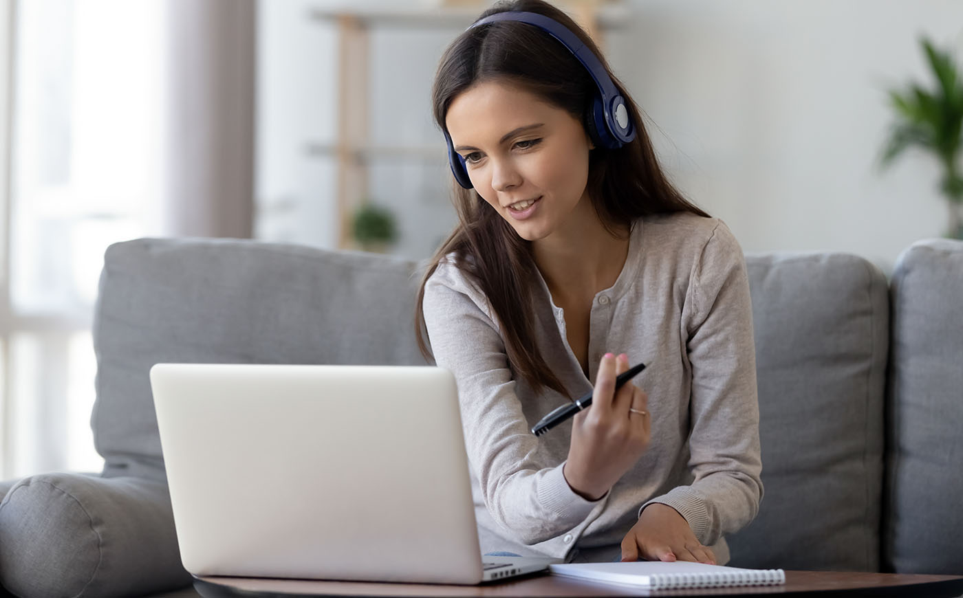 Young woman in headphones speaking looking at laptop making notes