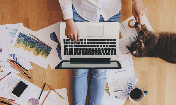 Person sitting on the floor surrounded by graph sheets, laptop, and cat