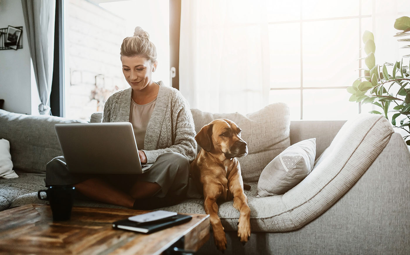 Woman working on laptop sitting at home with a dog via home office