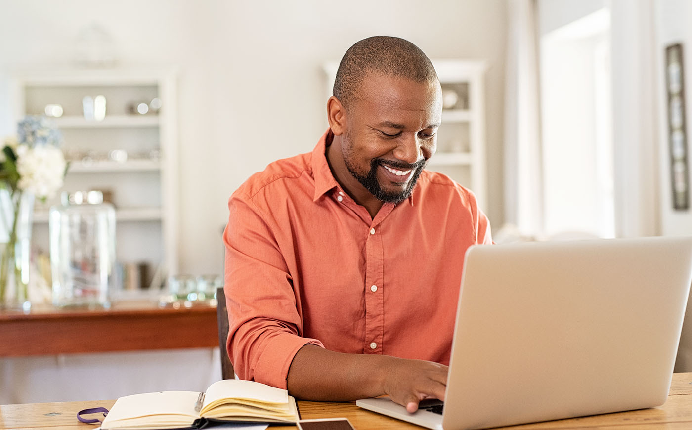 Smiling Black man using laptop at home in living room