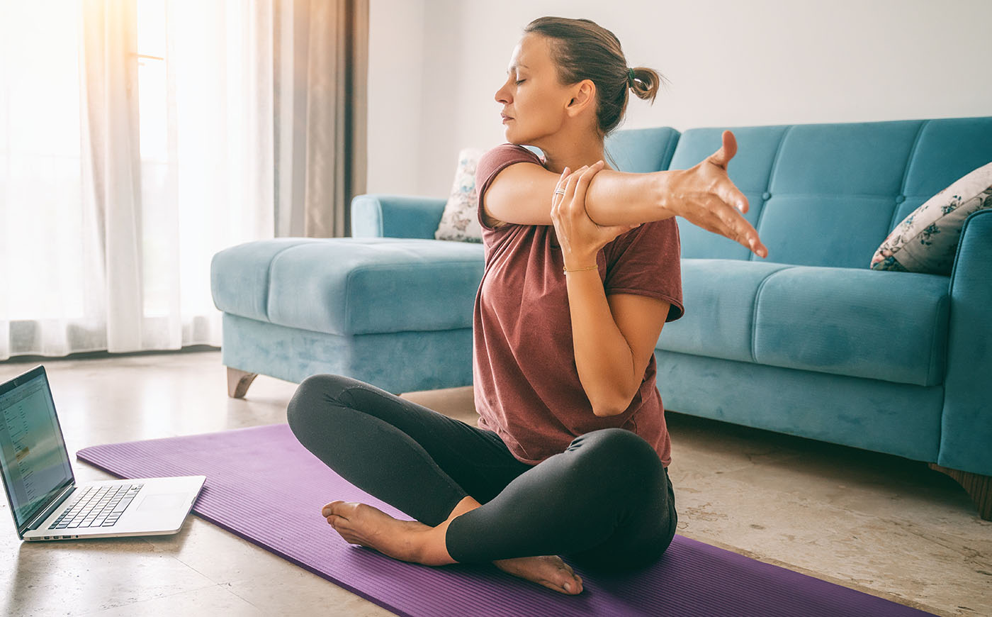 Young woman doing yoga stretching in front of yoga online class laptop at home