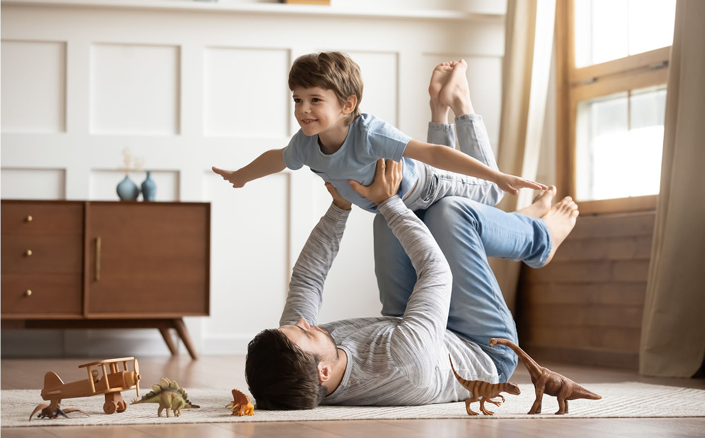 Father lying on carpet floor, lifting excited son in the air at home