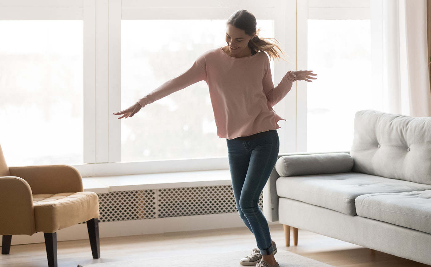 Young woman dancing in casual clothing in her modern living room in front of a window