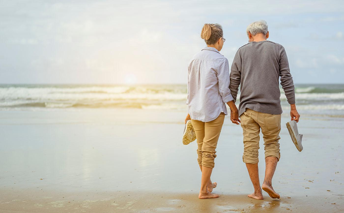 Old retired couple walking together hand-in-hand on the beach