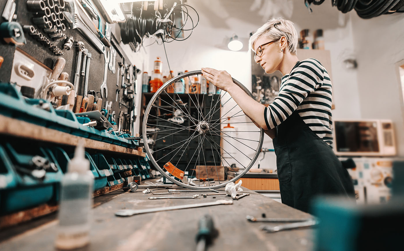 Young artistic woman crafts a bicycle wheel surrounded by tools in a workshop setting