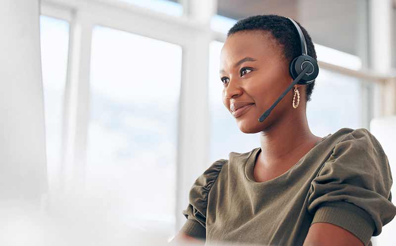 Young Black woman listens calmly to a customer on her headset in her home office