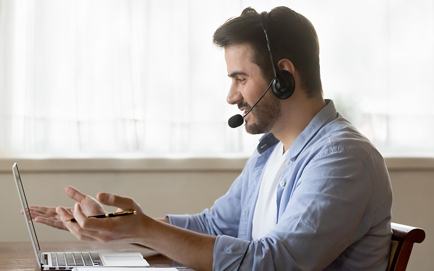Millennial customer service representative man has conversation wearing headset and working from home using laptop