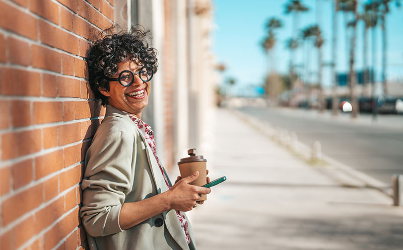 Mature Hispanic woman walking on the street, holding a coffee mug and smart phone