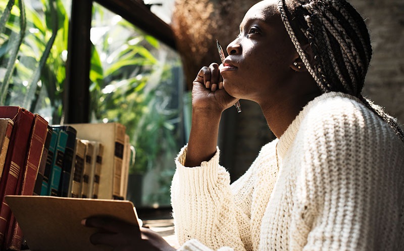 Black woman introspectively thinks about her words before she writes in her journal