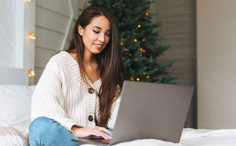 Young writer sits on her bed at holiday decorated home as she works on freelance writing work