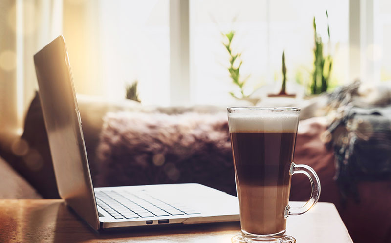 Cozy work desk sitting in the sunlight with a laptop and coffee latte with plants in the window