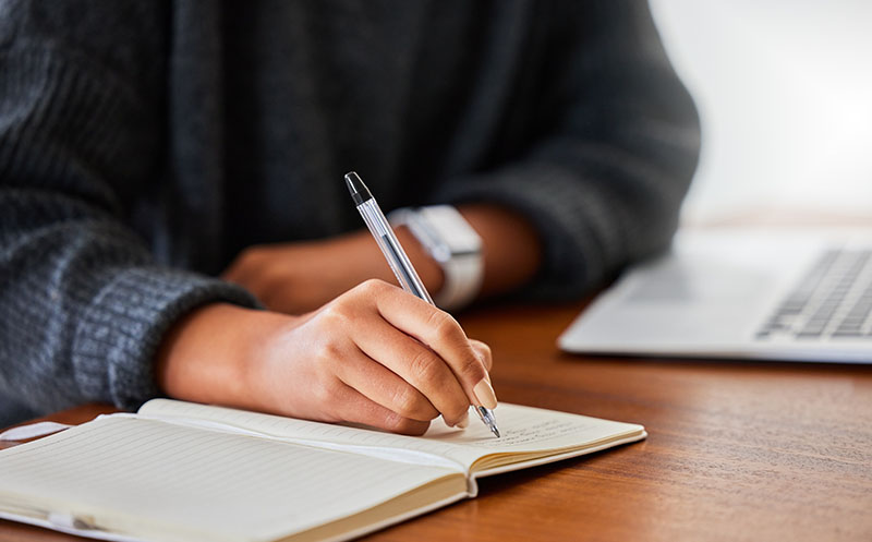 Close-up shot of someone journalling in a notebook while in front of their laptop