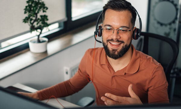 Happy entrepreneur wearing headset and using computer while working remotely in home office and having a video conference meeting