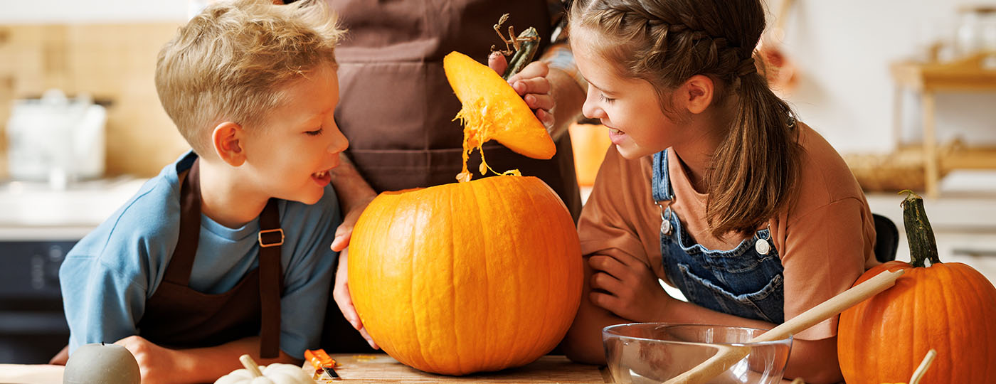 Two children laugh as a pumpkin is being carved in their home kitchen.