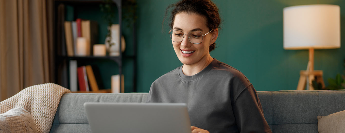 Woman sits on her couch at home, looking for independent contractor gigs on her laptop
