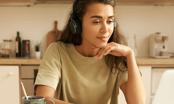 Stylish young Latin woman interpreter translating, wearing wireless headset, sitting at home in front of open laptop