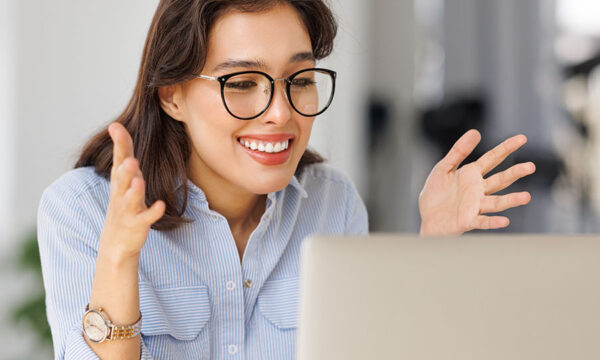 Woman converses virtually with someone on her laptop while she sits at home in her kitchen.