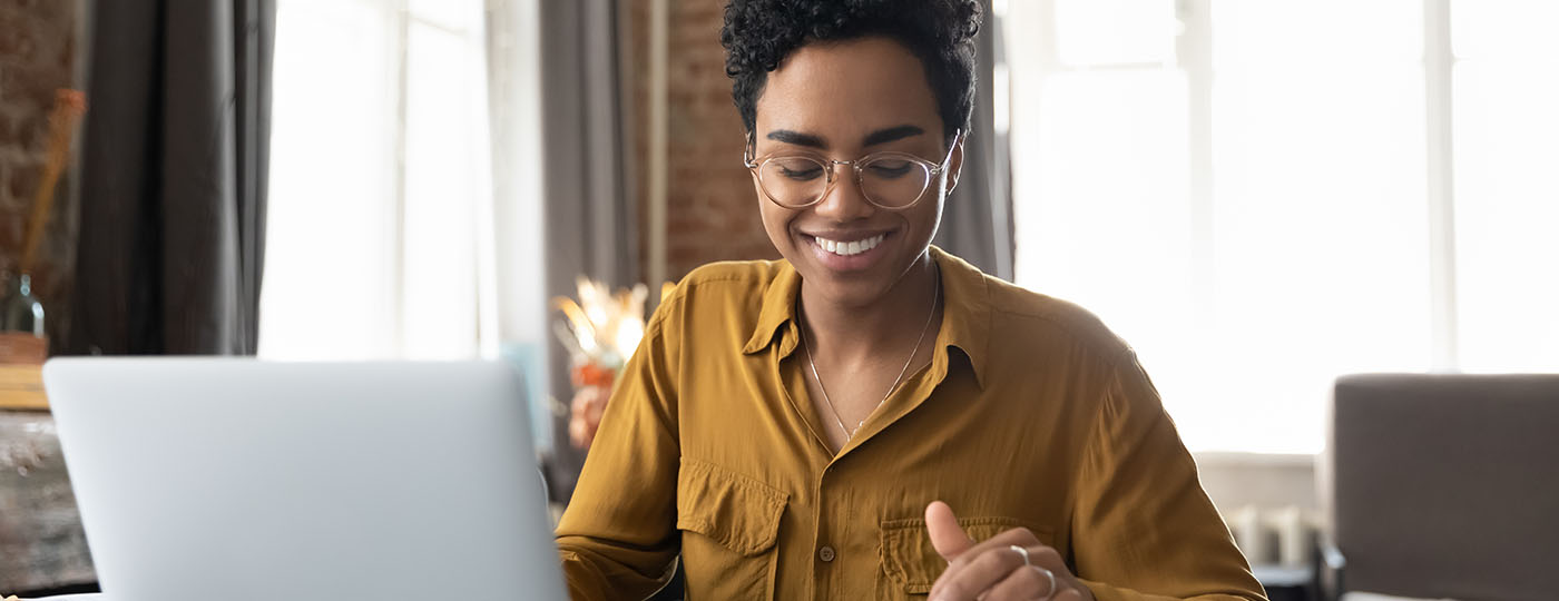 Young professional graduate smiles at her calculator as she answers a call as an agent representative on her laptop from home