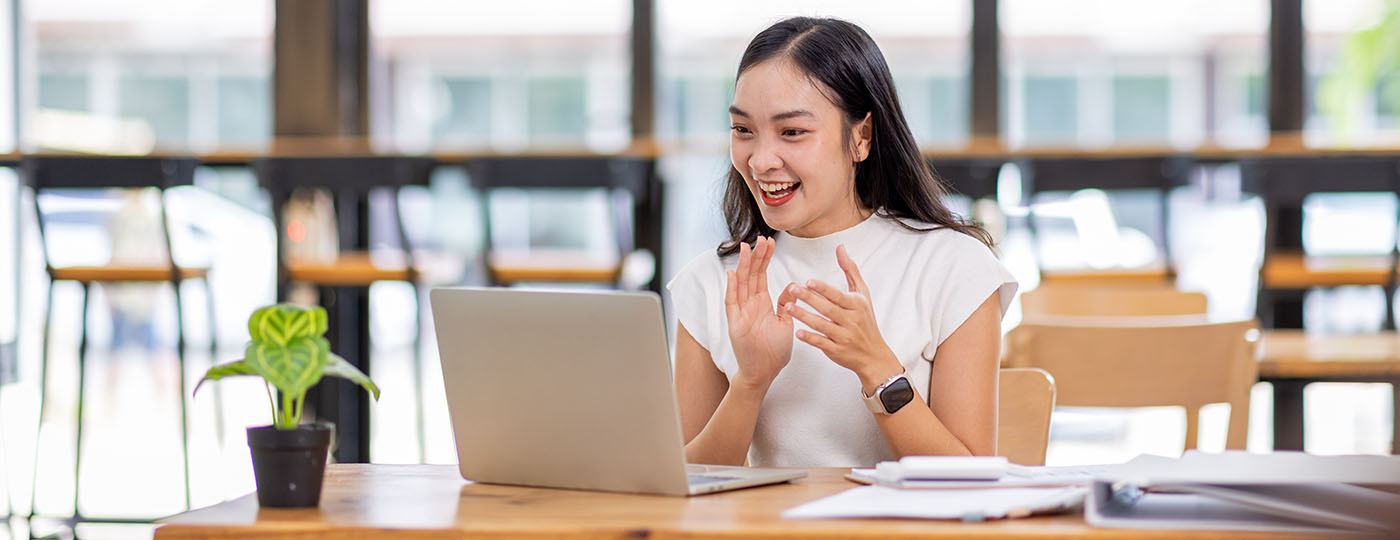 Professional individual chats enthusiastically to someone via her laptop in a cafe