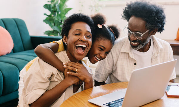 Parents and their child watching a video on a laptop, smiling and laughing