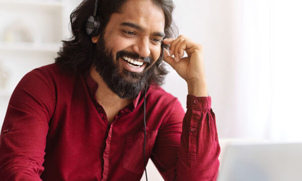 Smiling Young Indian Man In Wireless Headphones doing a pre-recoded interview on laptop at home